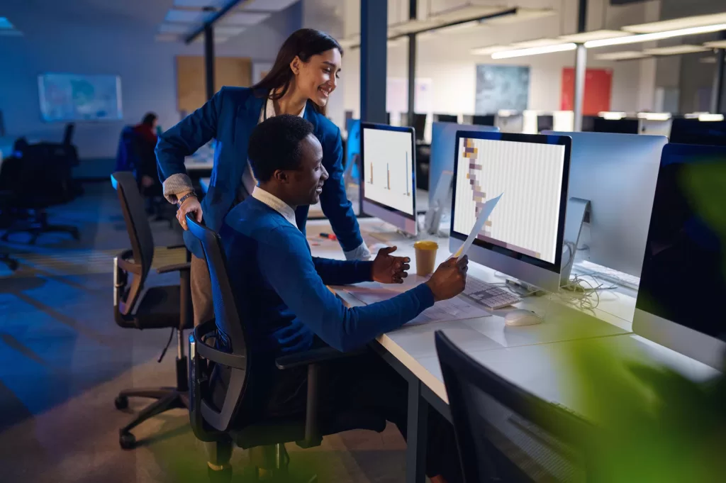 Two happy managers working in night office. Male and female workers, dark business center interior on background, modern workplace